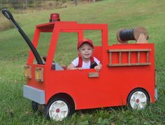 a little boy sitting in a fire truck made out of wood and fake grass on the ground