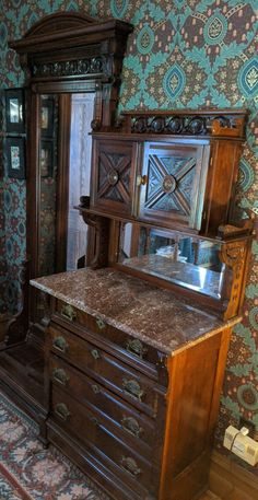 an old fashioned dresser and mirror in a room with floral wall paper on the walls