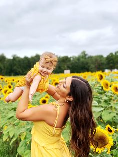 a woman in a sunflower field holding a baby up to her face and smiling at the camera