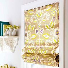 a window covered in yellow and white floral print roman shades next to bookshelves