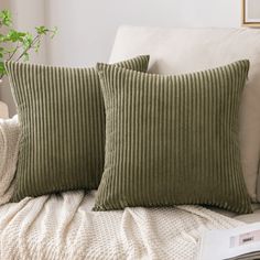 two green pillows sitting on top of a white couch next to a potted plant