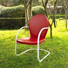 a red chair sitting on top of a green grass covered field next to a tree