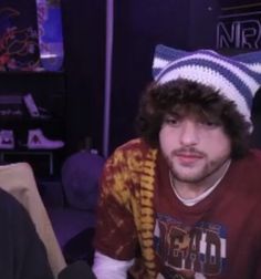 a man with long hair wearing a beanie and looking at the camera while sitting on a couch