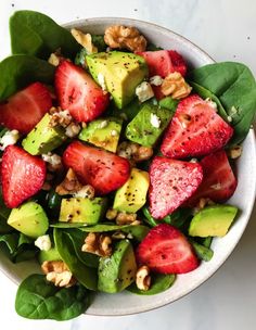 a salad with strawberries, avocado and walnuts in a white bowl