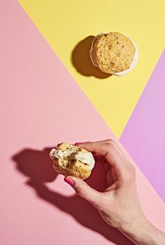 a person holding a cookie in their hand on a pink and yellow background with a half eaten one