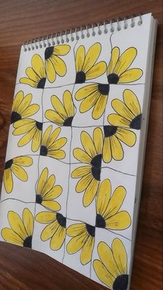 a notebook with yellow and black flowers drawn on it sitting on a wooden table next to a pen