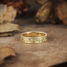 a gold wedding band with blue stones sits on a table next to leaves and flowers