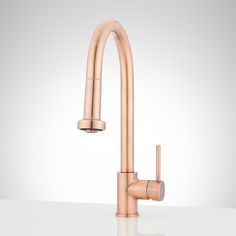 a kitchen faucet that is on top of a white countertop and has a rose gold finish