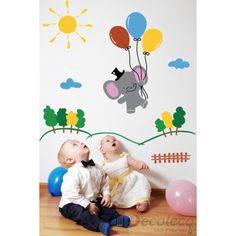 two babies sitting on the floor in front of a wall with balloons and an elephant