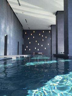 an indoor swimming pool with blue water and lights on the wall behind it, surrounded by tall columns