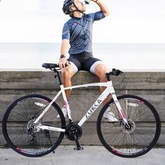 a man sitting on top of a bike drinking from a water bottle next to the ocean