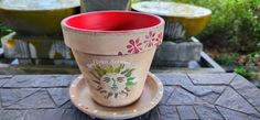 a red cup sitting on top of a saucer next to a planter filled with flowers