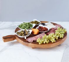 a wooden platter filled with meat, cheese and olives on top of a marble counter