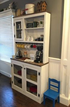 a white hutch with glass doors and shelves on the wall next to a blue chair