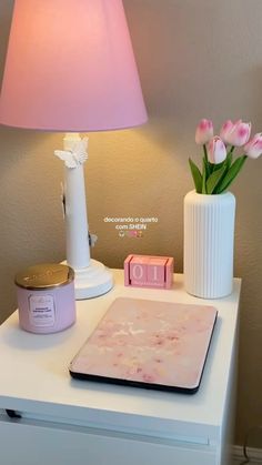 a table with a pink lamp and flowers on it next to a white desk top