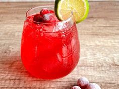 a red drink in a glass with ice and lemon wedges next to it on a wooden table