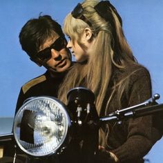 a man and woman standing next to each other on a motorcycle