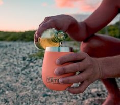 a person is pouring something from a bottle into a small cup while sitting on the ground