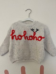 a sweater with the word hohoo written on it hanging from a hook in front of two hands