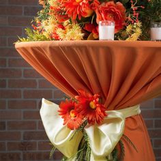 an orange table cloth with flowers on it and candles in the center is sitting next to a brick wall