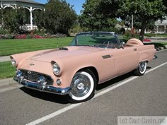 an old pink convertible car parked on the side of the road in front of a house