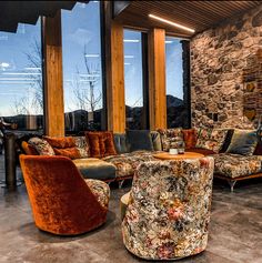 a living room filled with lots of furniture next to large windows on top of a stone wall