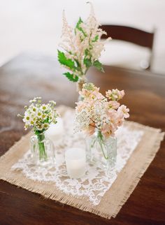 three vases filled with flowers sitting on top of a wooden table next to candles