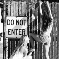 two young women standing next to a fence with a do not enter sign behind them