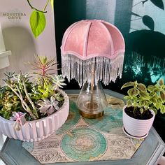 a pink lamp sitting on top of a table next to potted plants