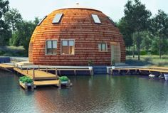 a round wooden structure sitting on top of a lake next to a dock and trees