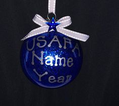 a blue ornament hanging from a white ribbon on a black background that says usa name year