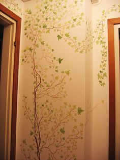 a bathroom with a tree painted on the wall next to a mirror and light fixture