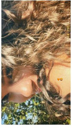 a close up of a woman's face with long hair and trees in the background