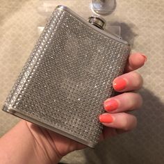 a woman's hand holding a silver flask with orange nail polish