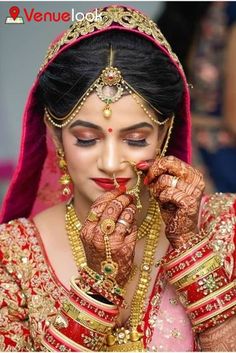 a woman in a red and gold bridal outfit is holding her hands up to her face