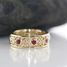 a yellow gold ring with two red stones on it and a rock in the background