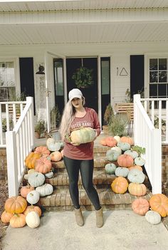 a woman standing on steps holding a plate of pumpkins in front of her house