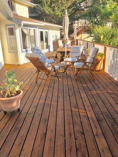 a wooden deck with chairs and an umbrella on it, next to a potted plant