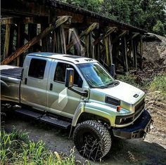 a silver truck is parked on the side of a dirt road next to a wooden bridge