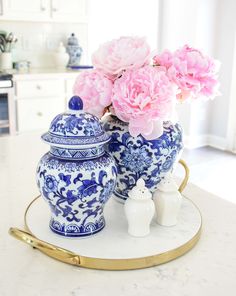 pink flowers are in blue and white vases on a gold tray with two smaller ones