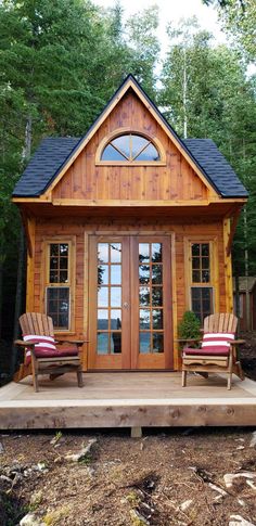 a small wooden cabin in the woods with two chairs on the porch and one chair sitting outside