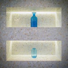 two blue vases sitting on top of shelves in a tiled wall next to each other