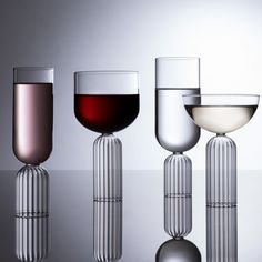 three wine goblets sitting next to each other on top of a reflective surface