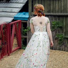 a woman in a white dress is walking away from the chicken coop with her back to the camera