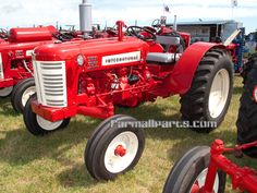 two red tractors parked next to each other on top of a grass covered field with people in the background