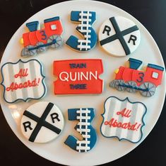 decorated cookies are arranged on a plate with train tracks and letters in the shape of trains