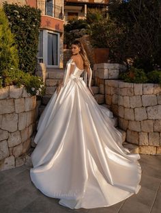 a woman standing in front of a stone wall wearing a wedding dress with long sleeves