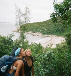 two young women hiking up a steep hill near the ocean, with trees and water in the background