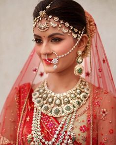 a woman wearing a red and gold bridal outfit with jewelry on her face,