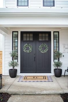 two wreaths on the front door of a white house with black doors and windows